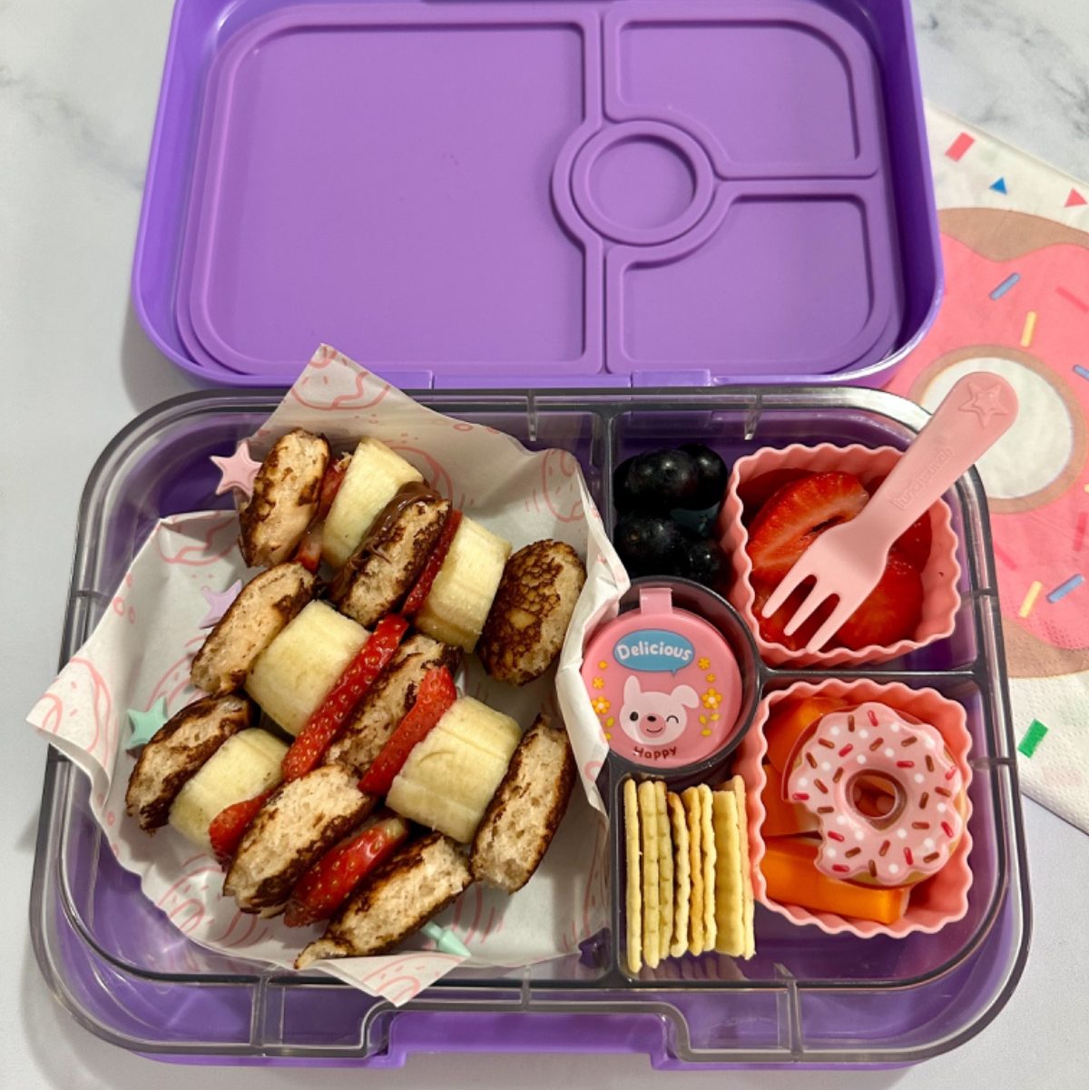 Banana strawberry pancake skewers in a purple lunchbox for a delicious kid's snack at school