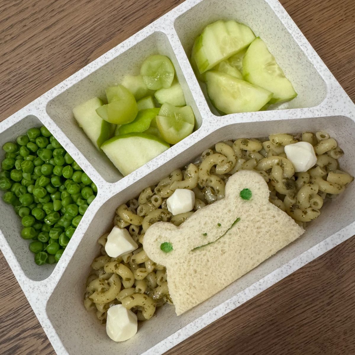 Fun lunchbox for a kid with a frog-shaped sandwich, and with green veggies and fruits.