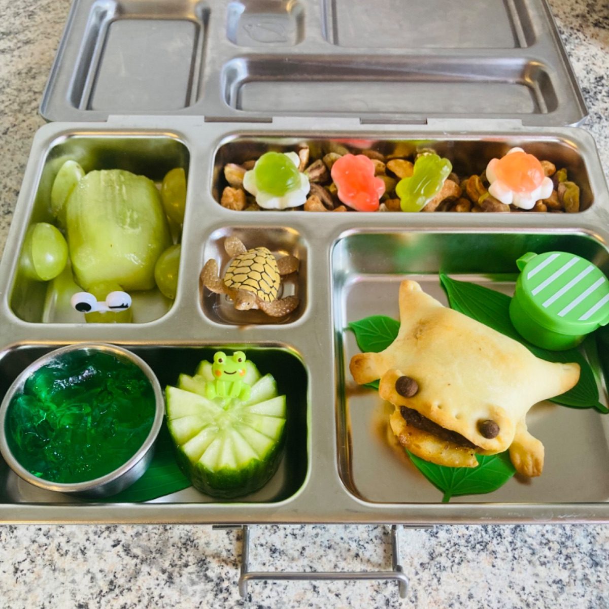Fun green-themed lunch with frog-shaped bun and kiwi-carved kiwi in a Plantebox stainless steel lunchbox for a kid
