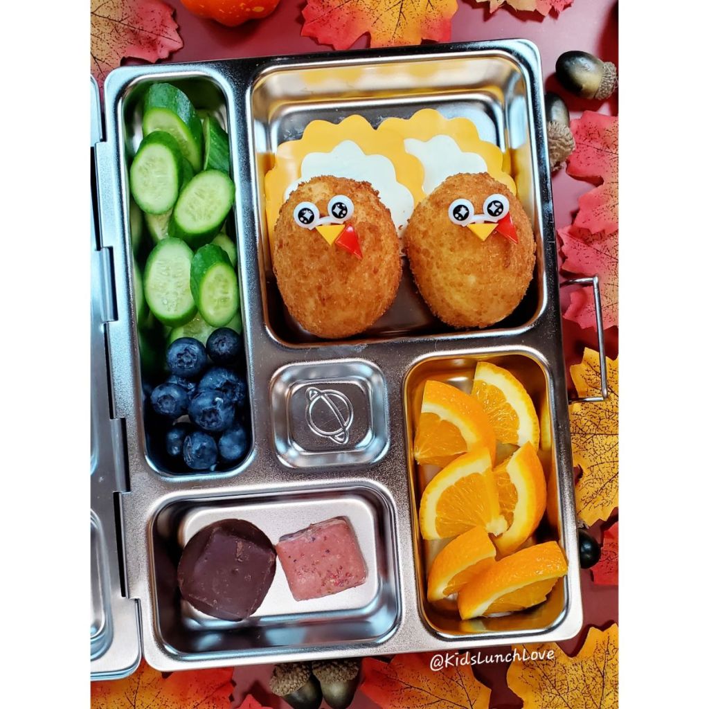 Cute corn dogs with fresh veggies and fruits in a stainless steel lunchbox for a kid's lunch at school.