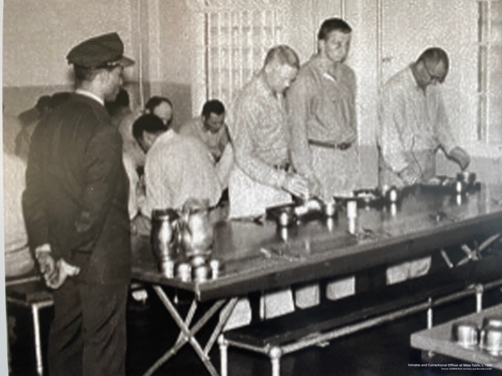 Historic photo of inmates eating in the Alcatraz dining hall with guards patrolling.
