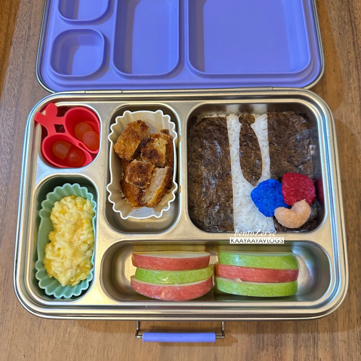 stainless steel kids' lunchbox with Squid Game salesman rice and green and red apple slices.