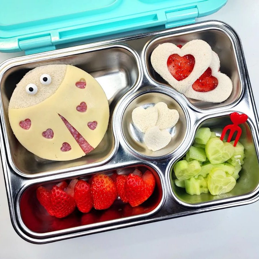 Valentine's Day lunch for kid with ladybug-shaped sandwich and heart-shaped fruits, veggies, and cookies.