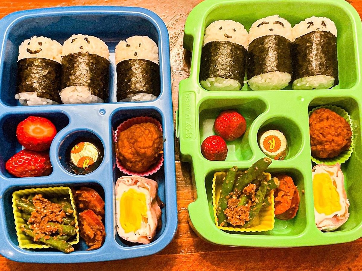 Healthy kids’ lunchbox with Japanese-style cylinder onigiri rice rolls filled with colorful vegetables and protein, packed in a bento box.