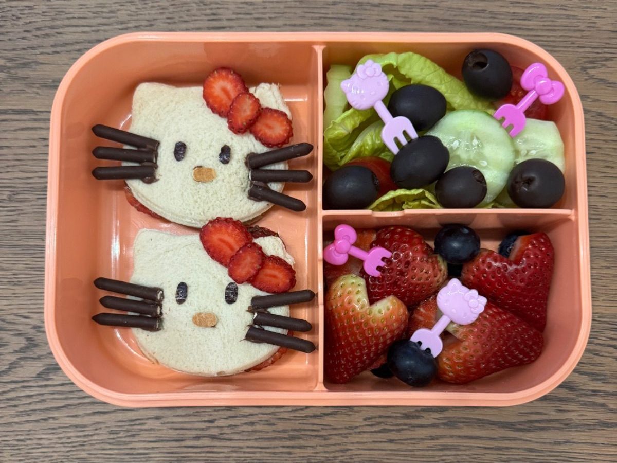 Hello Kitty-themed kids lunchbox featuring soft sandwiches with cheese bows and fresh berry accents in a bento-style container.