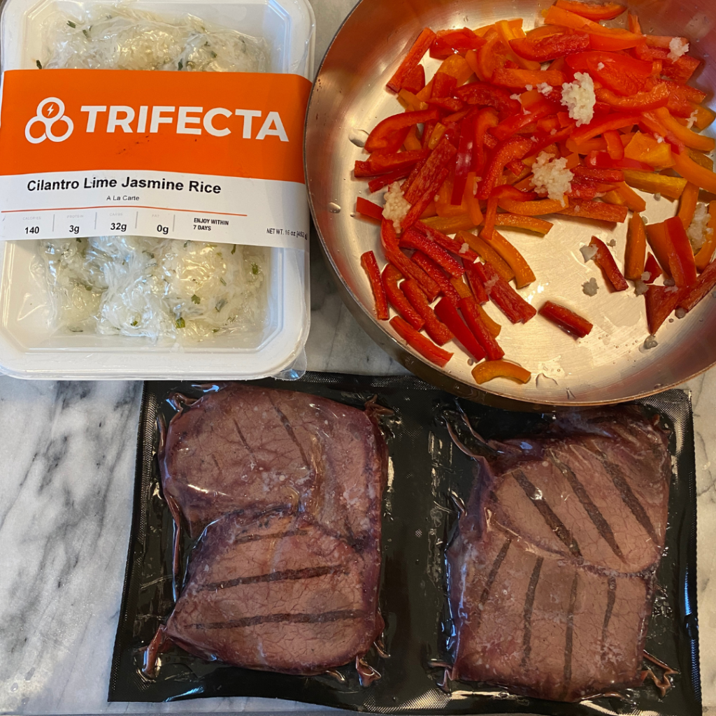 Trifecta meal prep with cilantro lime rice, seasoned beef steaks, and fresh vegetables packed in a lunchbox for kids and teens school lunch by Teuko.
