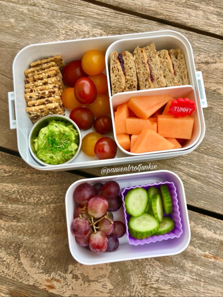 Guacamole, crackers, mini PBJ sandwiches, and fresh fruits and veggies in a bento lunchbox, for a kid's lunch at school