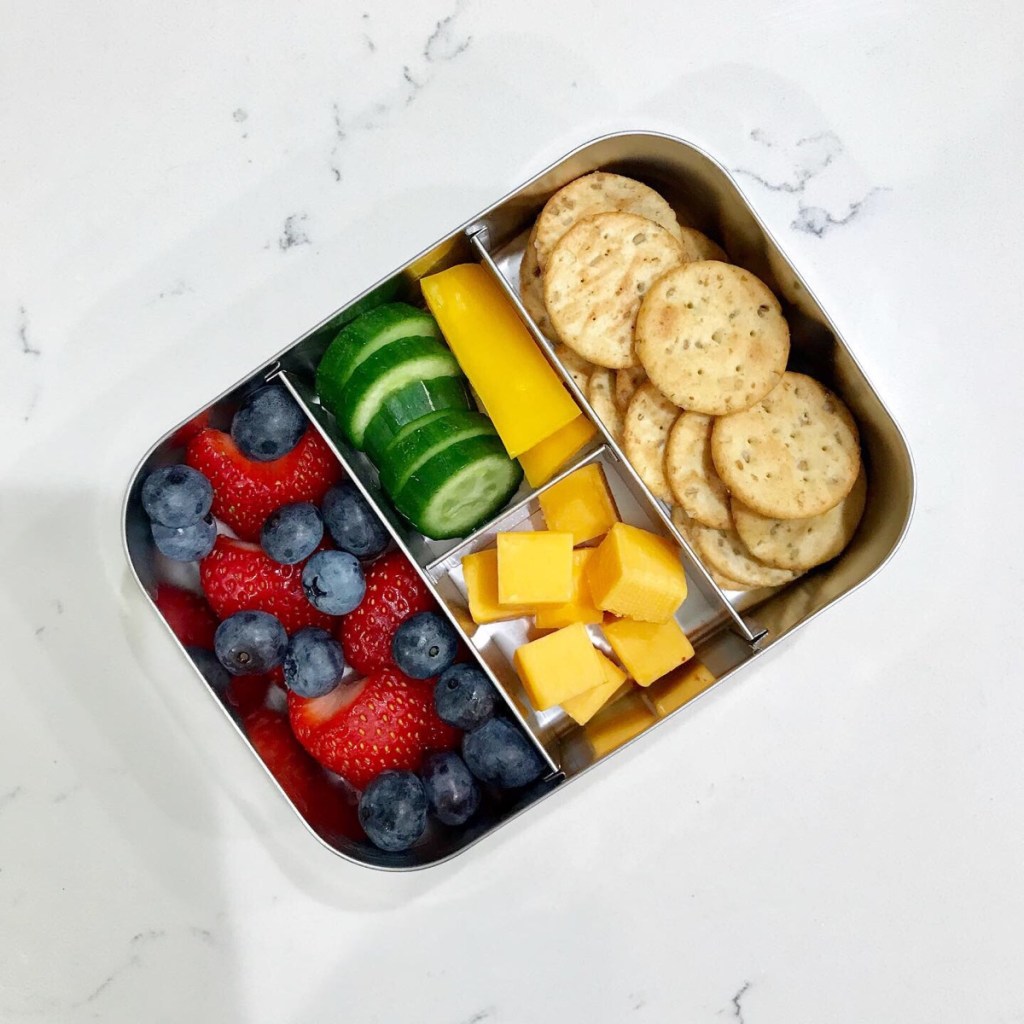 Cheese, crackers, and fruits and veggies in a kid's stainless steel snack box