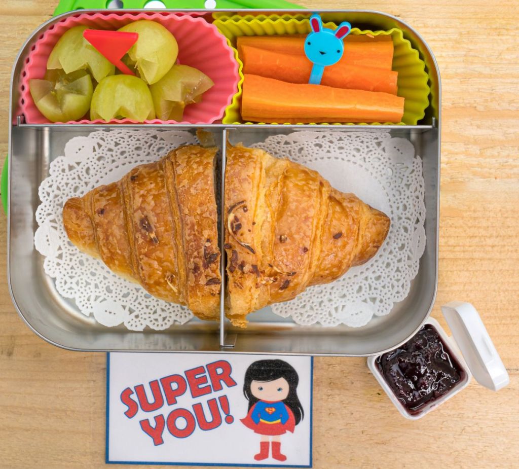 Grapes, carrot sticks, and a croissant sandwich in a kid's bento lunchbox