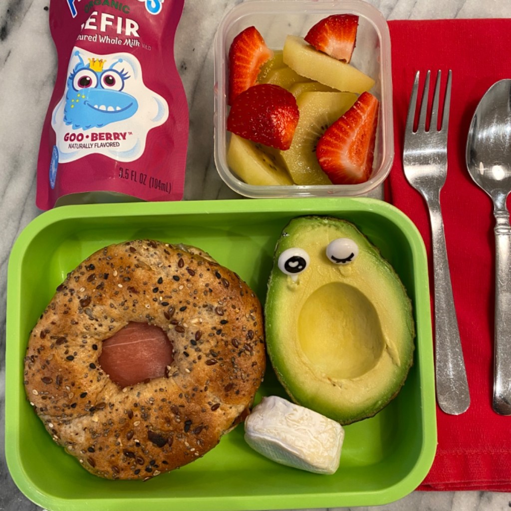 Bagel sandwich, avocado, kefir, and fruit salad for a kid's lunch packed for school