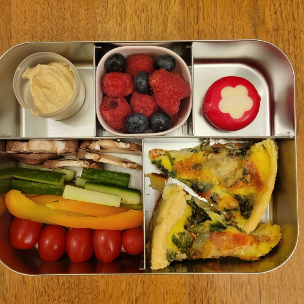 Hummus, veggies, and mini slices of quiche in a stainless steel Lunchbox bento lunchbox for a kid's lunchtime at school