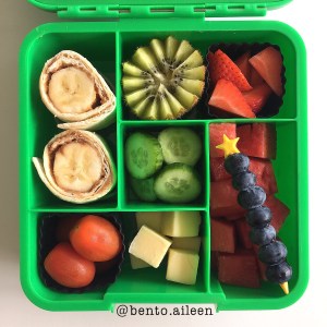 Peanut butter and banana rolls with fruits and veggies for a kid's lunch in a bento box sent to school