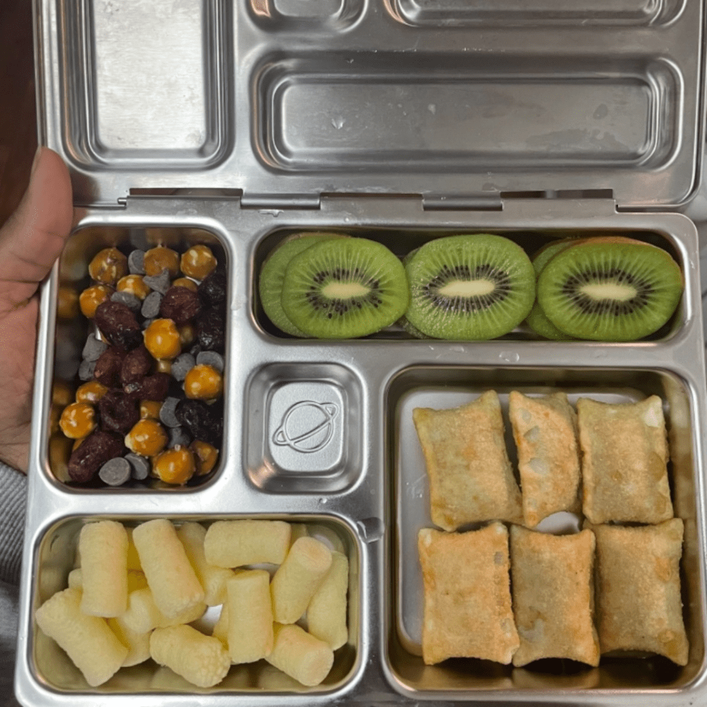 Teuko Lunchbox Community.In a Planetbox bento box, she put six pizza roll-ups, some cheese puffs on the side, and sliced kiwis. For the trail mix, she mixed, mini pretzel balls, chocolate chips, and dried cranberries.