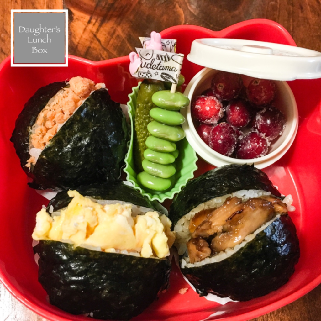 Teuko Lunchbox Community. lunchbox with three different stuffed rice balls (the first one is filled with salmon, the second one with scrambled egg, and the last one with chicken cotaed in yakitori sauce.... yum!), a mini skewer of edamames, one small pickle... and a tiny snack box filled with a few sugared cranberries.
