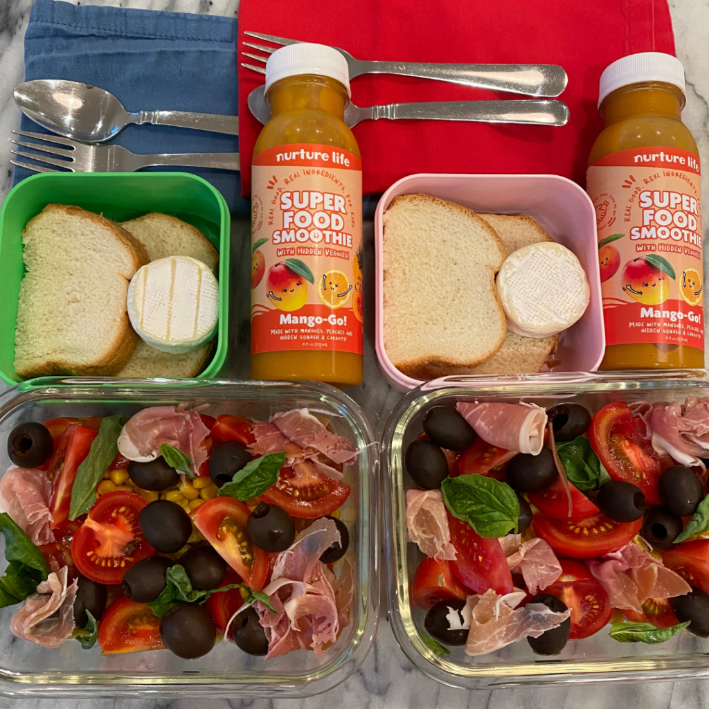 A kids' lunchbox idea with a summer salad made out of tomatoes, corn, black olives, basil and prosciutto. bread and mini brie. Mango smoothie for dessert or snack.