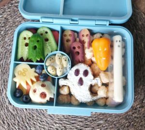 Ghost veggie dippoers like carrot slices and cucumber slices in a Halloween themed lunchbox for a kid's school lunch